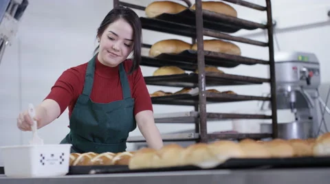 4K Happy young worker in bakery kitchen brushing glaze onto buns Stock Footage