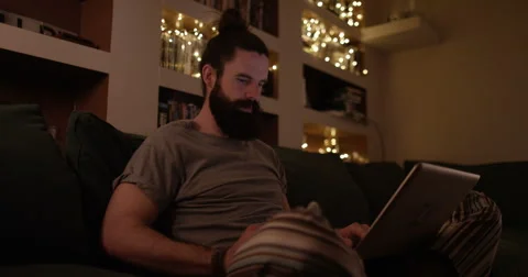 4K Hipster guy relaxing at home at night, streaming film or TV show on laptop Stock Footage 68073784