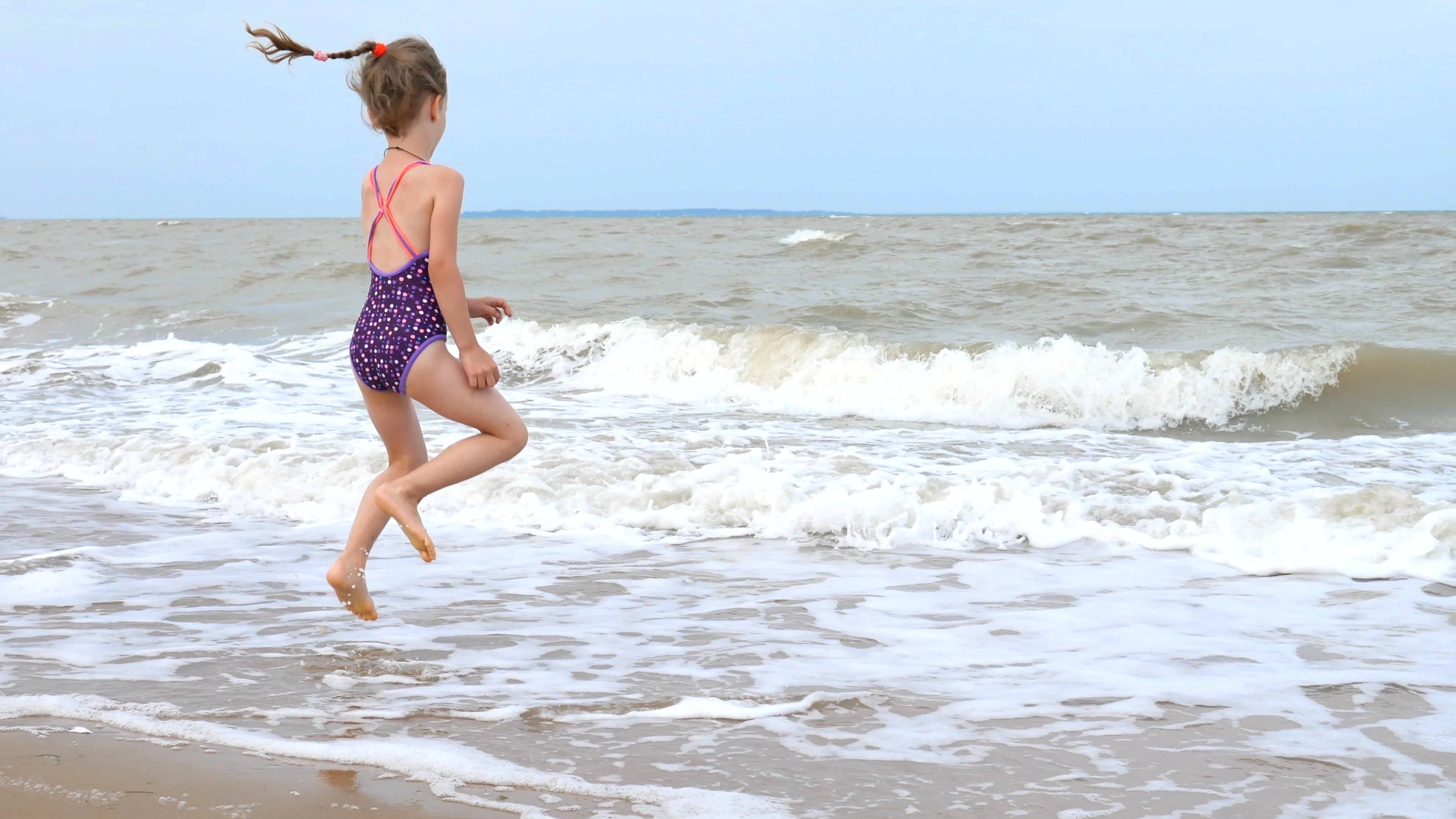 4K. A little girl in a swimsuit is playing with waves on the ocean shore. At sea