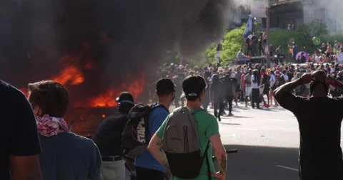 4K LONG SHOT CAR ON FIRE WITH PROTESTERS Stock Footage 131454710