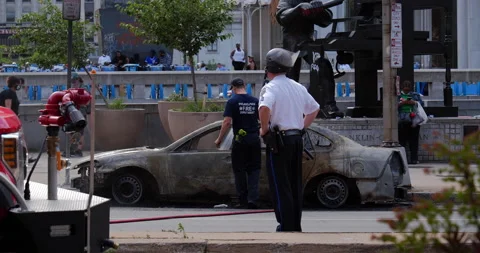 4K LONG SHOT OF A COP OBSERVING A FIREFIGHTER HOSING VANDALIZED CAR Stock Footage 131457825