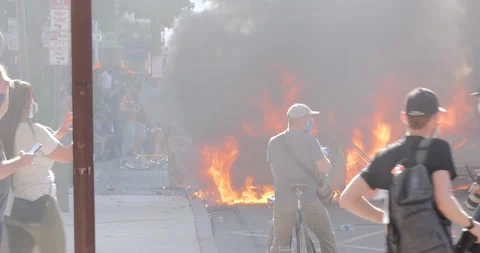 4K LONG SHOT OF FIRE WITH PROTESTERS IN THE FOREGROUND Stock Footage 131454007