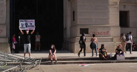 4K LONG SHOT PROTESTERS SITTING ON STEPS WITH SIGN Stock Footage 131454027