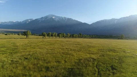 4k Low altitude reverse POV over green pastures with mountains at sunset. Stock Footage 87299329
