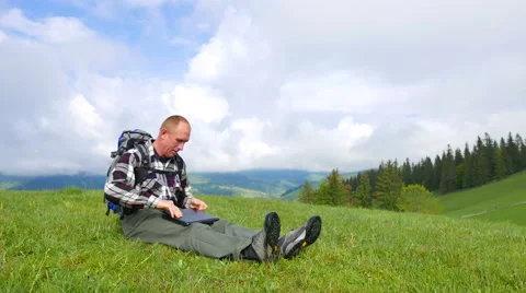 4K  Man backpacker in mountains with portable computer received good news Stockbeeldmateriaal 64007837