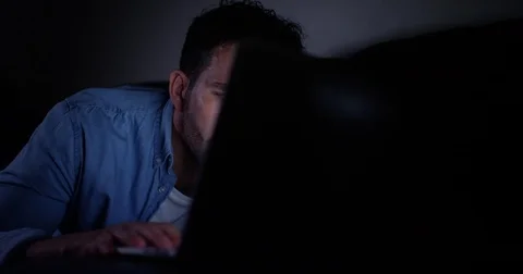 4K Man with laptop on the couch at night concentrating on what he sees on screen Stock Footage 80076526
