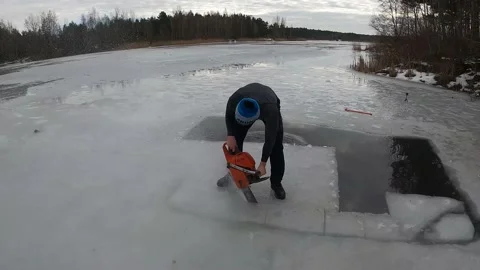 4K man sawing ice hole with a chainsaw in winter for swimming on a lake Stock Footage