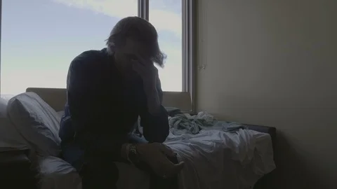 4K Man Sitting on Bed Near Window Depressed Running Hand Through Hair Stock-Footage 100799588