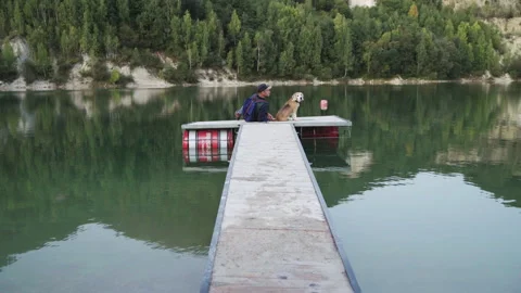 4K Man sitting with his beagle on wooden pier contemplating lake in autumn Stock-Footage 158930787