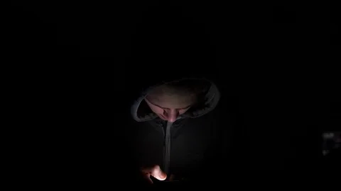 4K Man on a smart phone with light on face, laughing. hooded teen with a dark 库存影片 90795727