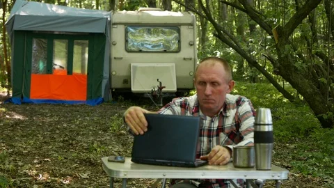 4K. Man traveler work at  notebook  near trailer in wood. Freelance team Stockbeeldmateriaal 95403256