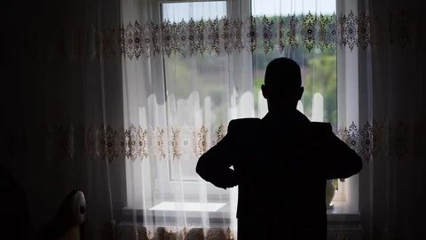 4k Man wearing and buttoning shirt near window silhouette Stock Footage 107774237