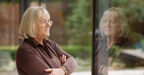 4K Mature woman deep in thought, staring out of hospital window waiting for news Stock Footage