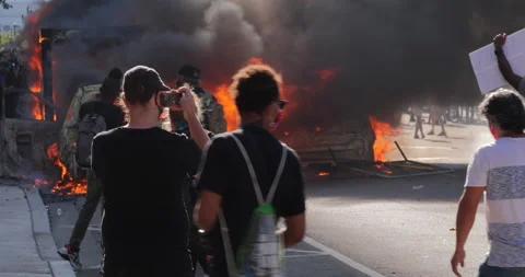 4K MEDIUM SHOT CAR BURNING WITH PROTESTERS WATCHING Stock Footage 131454121