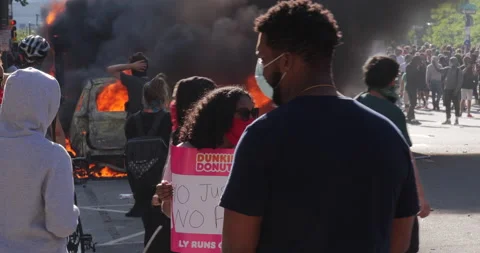 4K MEDIUM SHOT CAR ON FIRE WITH PROTESTERS WATCHING Video stock 131454065