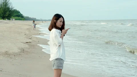 4K, medium shot A young Asian woman on the beach using her mobile phone to se Stock Footage 201202069