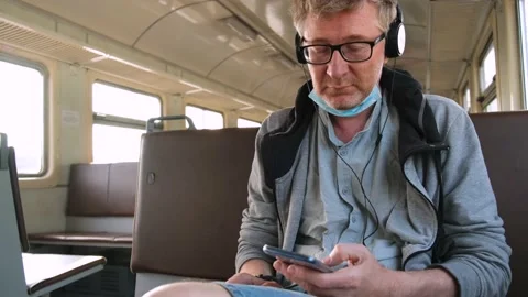 4K A middle-aged man is sitting on public transport with headphones and a phone. Stock Footage 159598611