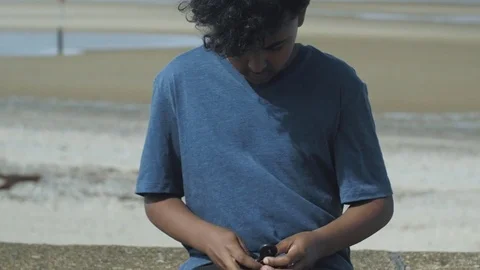 4K Mixed Race Young Boy Spinning and Dropping Toy on Sunny Beach 库存影片 75956185