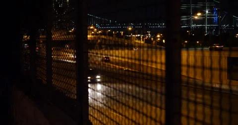 4K NIGHT STATIC HIGHWAY SHOT THROUGH WIRE FENCE WITH BRIDGE IN BACKGROUND Stock Footage 131281143