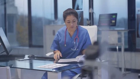 4K Nurse in modern hospital studying patient x rays & working on computer Stock Footage