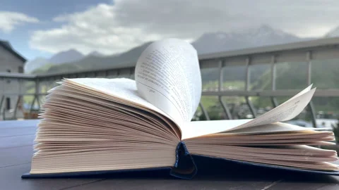 4K open paper book sitting on table on outside terrace with wind stirring pages Vidéo 213162626