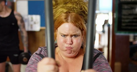 4K Overweight woman pulling faces, straining to use weights machine at the gym Stock Footage 94836399