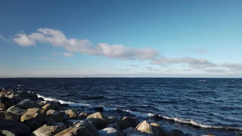4K, Pan of ocean, waves and rocky shore, clouds in blue sky. Oresund bridge Stockbeeldmateriaal 147194193