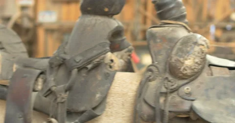 4K Pan of Old west used worn antique western saddles displayed on wall Stock Footage 54469064