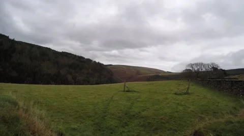 4K Pan of tree covered hills and green fields with grey and white clouds Stock Footage 45623835