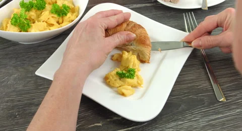 4K: A portion of scrambled eggs together with a croissant is laying on a plate Stock Footage 65760658