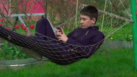 4K Portrait boy Playing Tablet in Hammock, the young man Face Use Smart Phone in Stock Footage 75915331