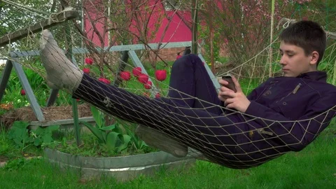 4K Portrait boy Playing Tablet in Hammock, the young man Face Use Smart Phone in Stock Footage 75918049