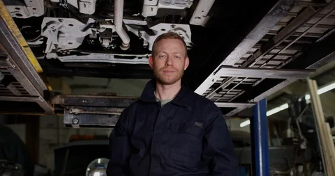 4K Portrait mechanic standing under car in workshop, successful business owner Video stock 112576410