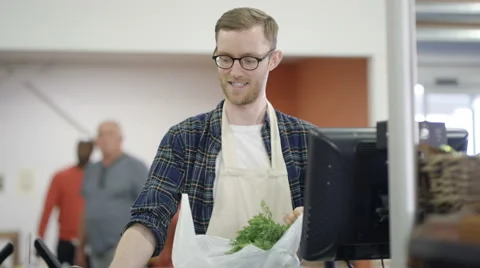 4K Portrait smiling grocery store worker packing customer's bag at the checkout Stock Footage 67907920