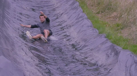 4K Portrait smiling mud race runners after slide down hill into cold muddy water Stock Footage 66044966