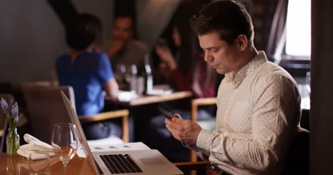 4K Professional man working on laptop &amp; talking on phone in relaxed bar setting Stock Footage 62897386