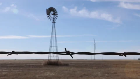 4K Rack focus to barbed wire from an old windmill and modern windmill in Texas Stock Footage 229521558