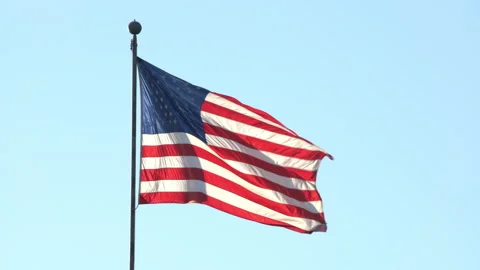 4K real time long shot of a backlit American flag waving in a clear blue sky Stock Footage 139541344