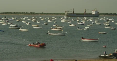 4K red camera, SM Cargo ship in background passing behind fishing boats on beach Stock Footage 75424154