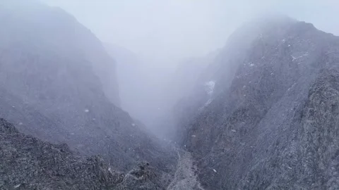 4K reverse drone flying backward in snowy mountain valley with fog Stock Footage 336449606