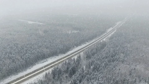 4K. Road in the winter forest with driving cars at snowfall. Aerial view. 動画素材 79159272