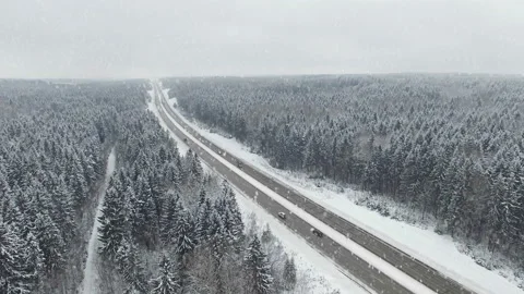 4K. Road in the winter forest with driving cars at snowfall. Aerial view. Video stock 99375094