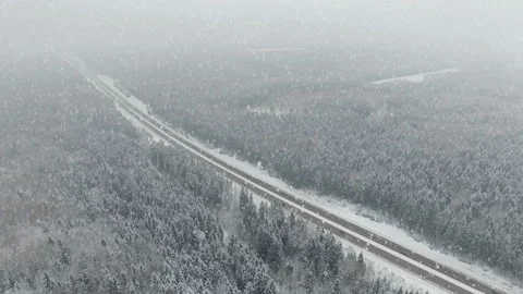 4K. Road in the winter forest with driving cars at snowfall. Aerial view. Video stock 99375681