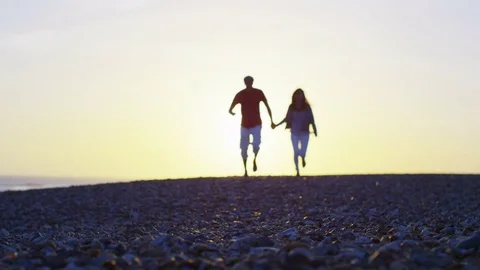 4K Romantic young couple holding hands & running on the beach at sunset Stock Footage