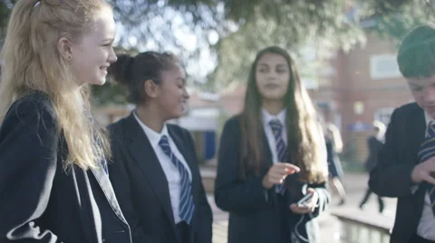 4K School children using mobile phones with earphones outdoors in playground Video stock 60675477