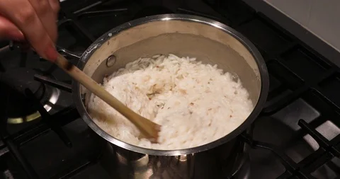 4k shot overlooking a pot of stirring rice one a stove with wooden spoon Stock Footage 90876992