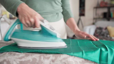 4K shot of woman's hands using a steam iron to smooth wrinkles from green fabric Video stock 318106987
