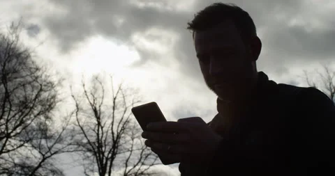 4K Silhouette of isolated man using smartphone outdoors in the park Vídeo Stock 107314507