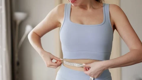 4K slow motion close up of young woman measuring waist with tape at home in M Stock Footage 329301093