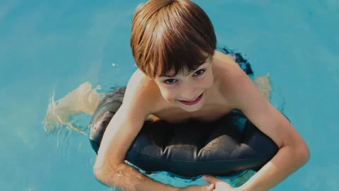 4K slow motion of a happy boy swimming with an inflatable float in a blue poo Stock Footage 342663618